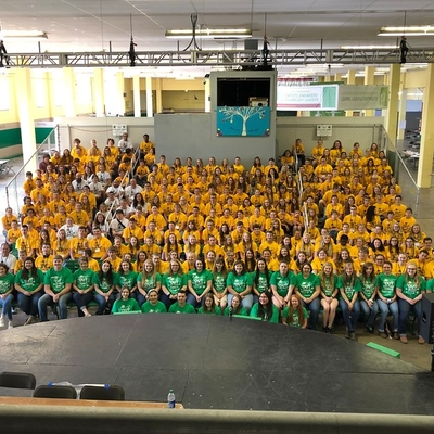 A large group of youth sitting on bleachers wearing yellow and green shirts. 