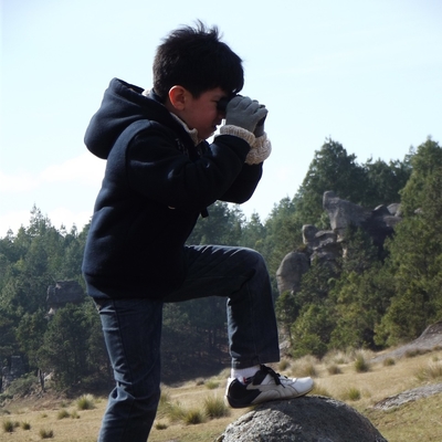 A boy standing on a rock with binoculars up to his face