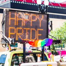 A neon sign reading Happy Pride is on top of a truck in the parade.