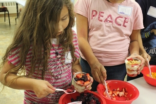 A girl and a woman stand in line filling their yogurt parfaits with fruit. 
