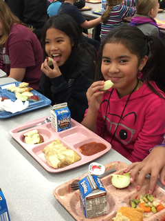 Two elementary student eat a healthy lunch including Minnesota grown apples. 