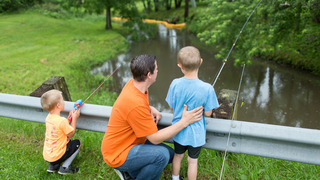 A father and two sons fishing over a bridge.