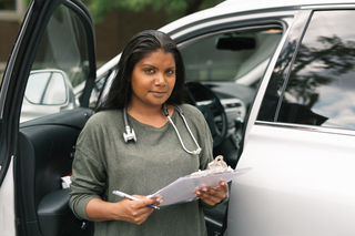 Native American medical professional holding a clipboard by her car
