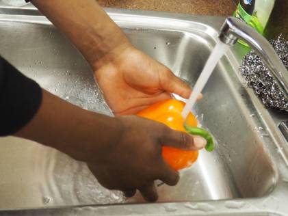 hands holding an orange pepper under running faucet